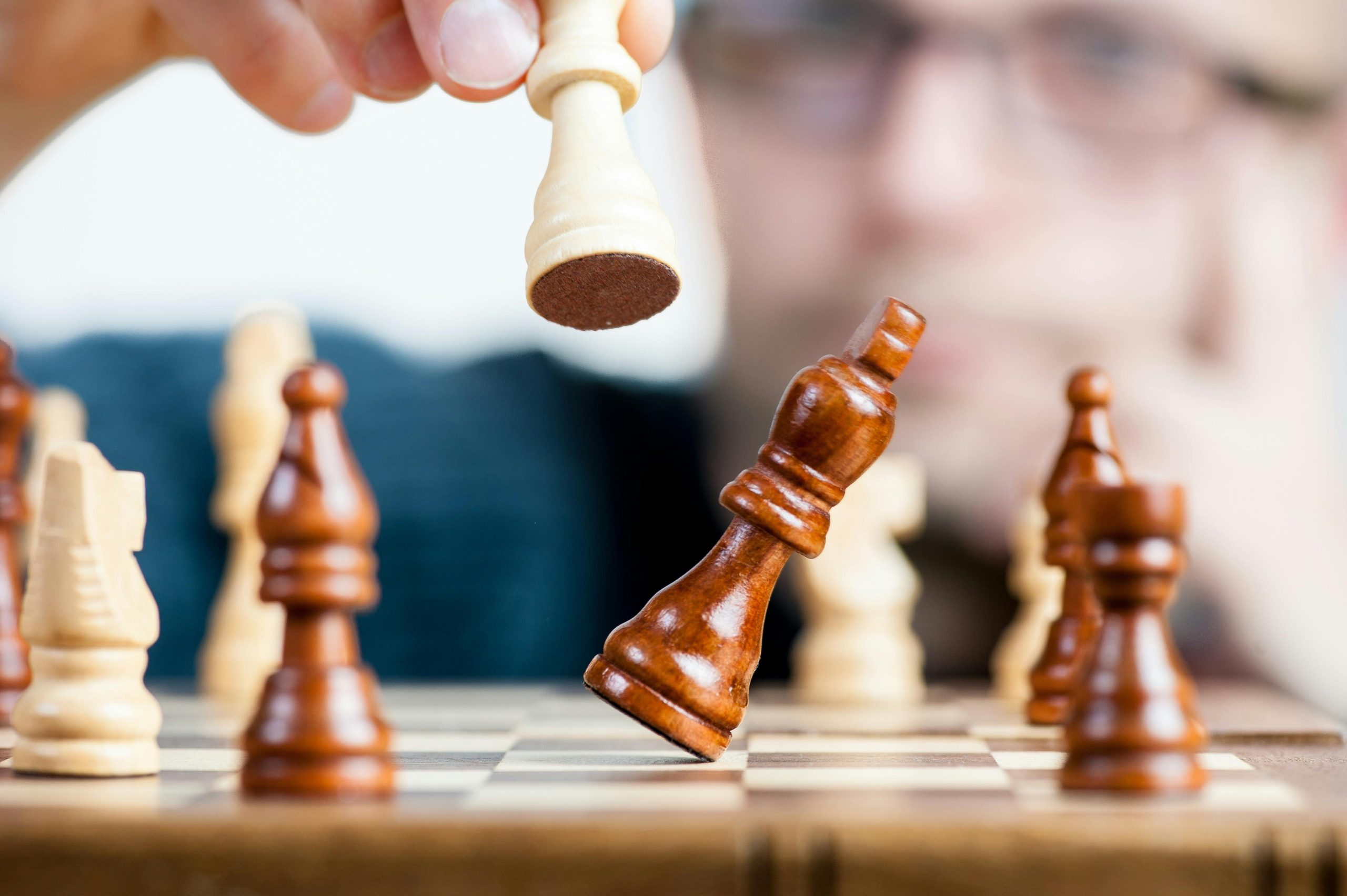 Az ember stratégiailag megmozgat egy fehér sakkfigurát, szimbolizálva a játékban való mesterségét, hasonlóan az online marketingszolgáltatásoknál megkövetelt precizitáshoz. Az elmosódott háttér és a fókuszált előtér kiemeli a folyamatban lévő játékot.