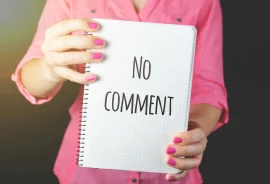 Egy rózsaszín pólós nő áll, kezében egy füzetet tart, amin a "No comment" felirat olvasható.