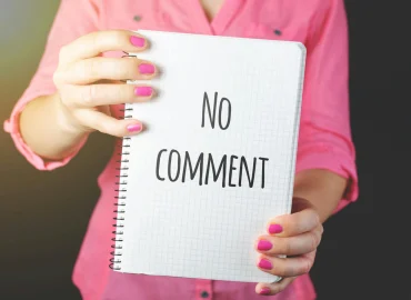 Egy rózsaszín pólós nő áll, kezében egy füzetet tart, amin a "No comment" felirat olvasható.
